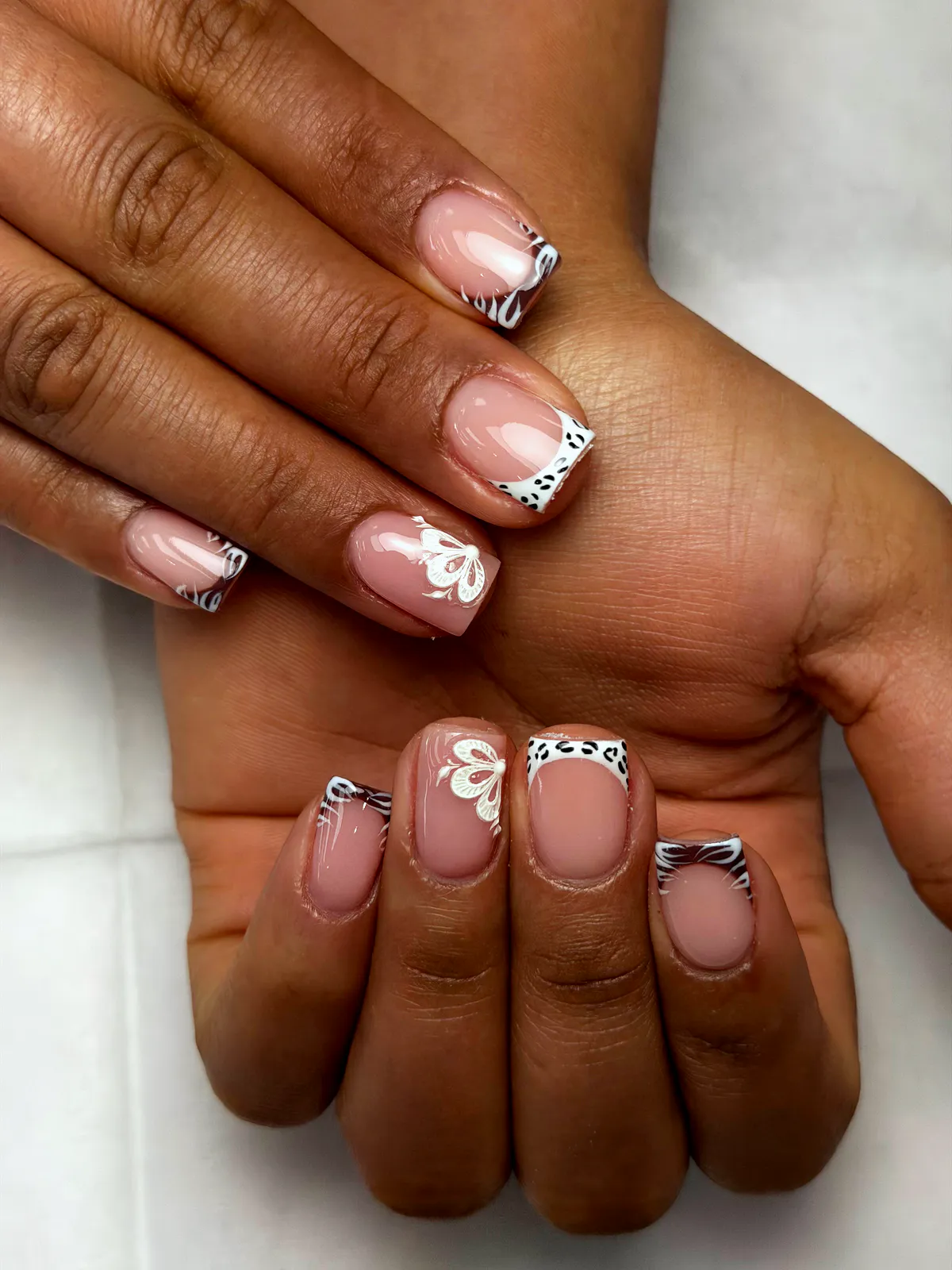 Short square nude French nails with black-and-white animal-print tips and small white flowers, by BeautyFusionClau in Sarasota, Florida