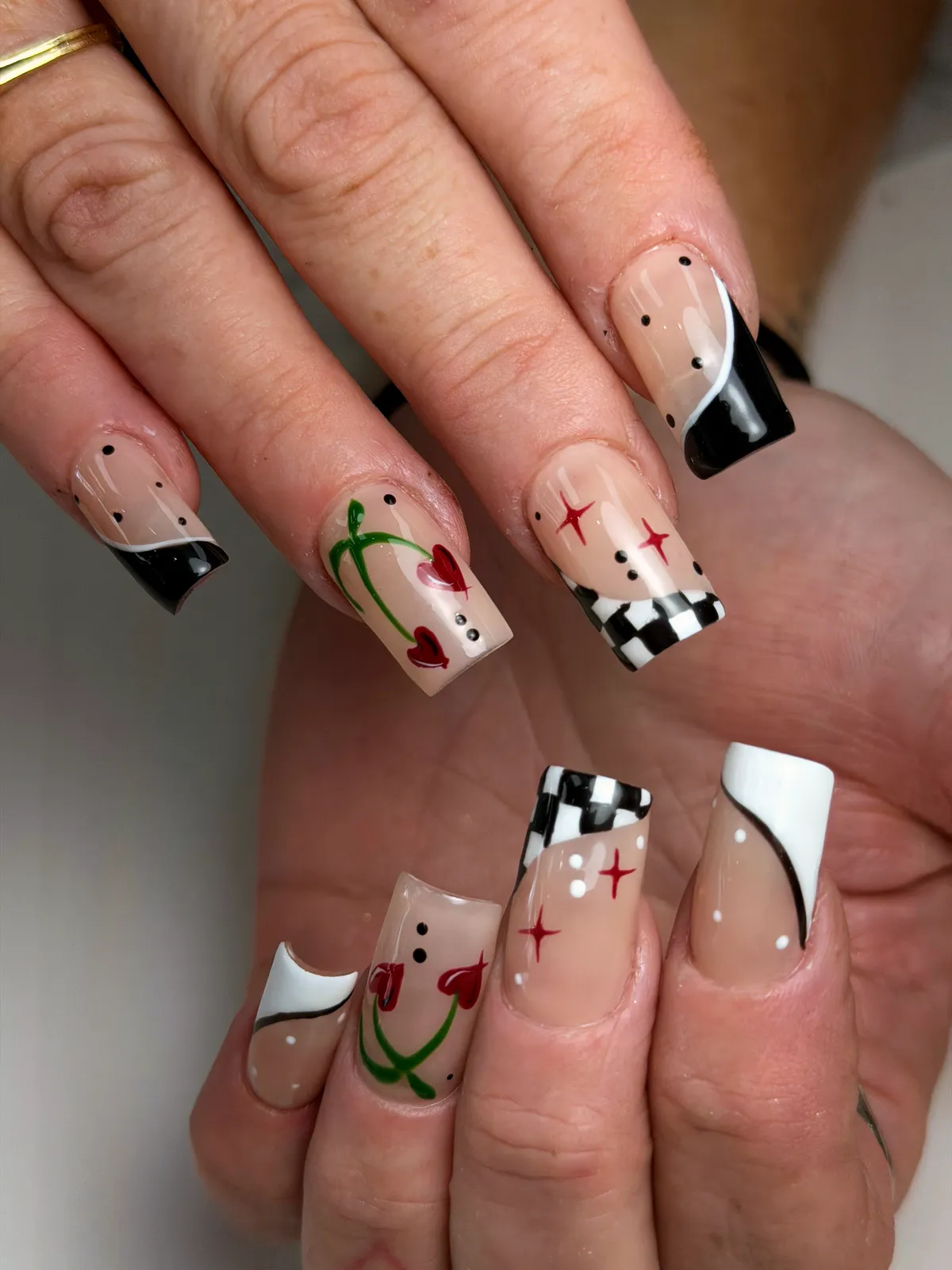 Square nude nails with black-and-white swooshes, a checkerboard, red hearts and red stars, by BeautyFusionClau in Sarasota, Florida