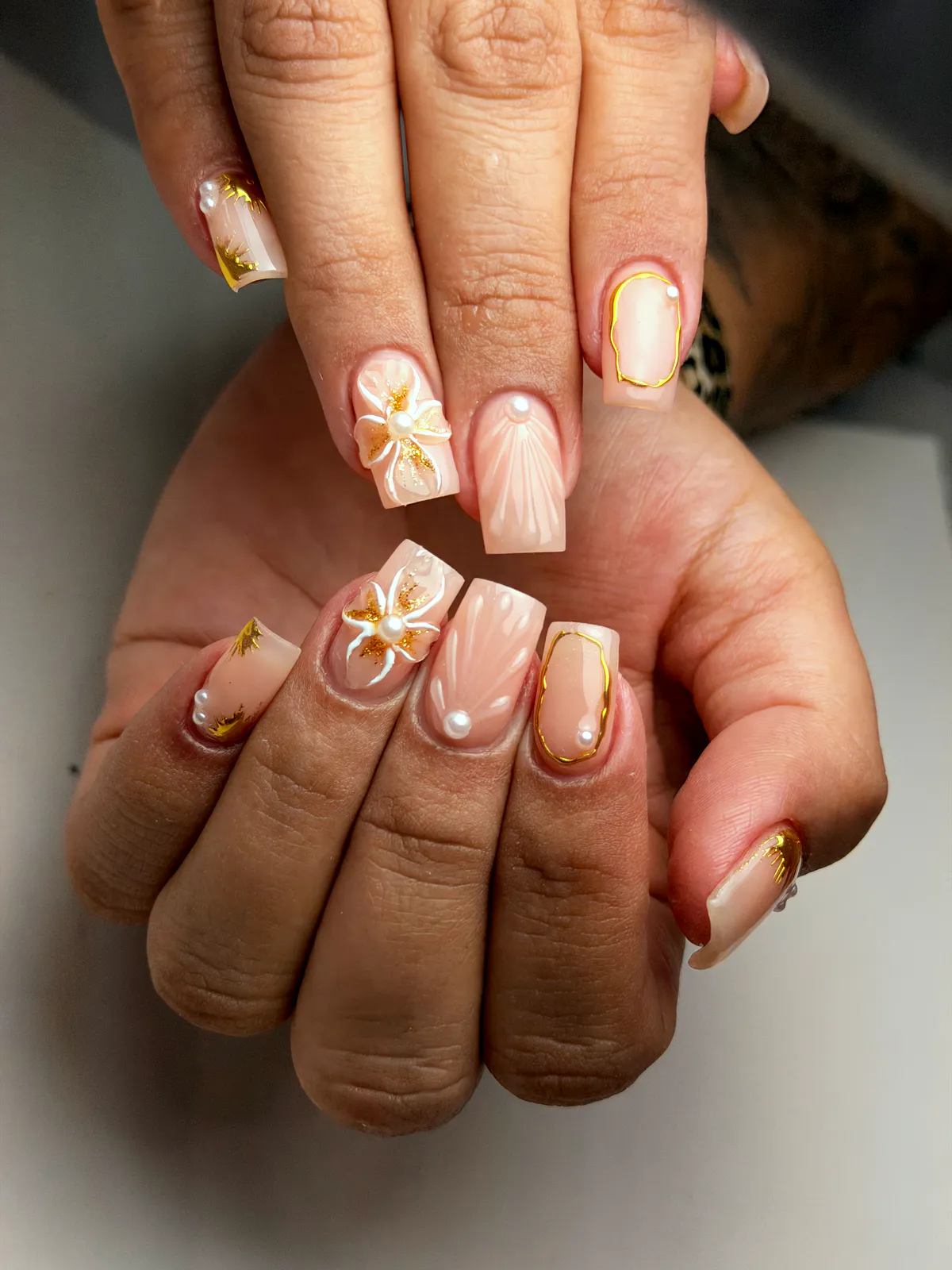 Sheer peach square nails with gold frames, pearls and a white flower with gold leaf, by BeautyFusionClau in Sarasota, Florida